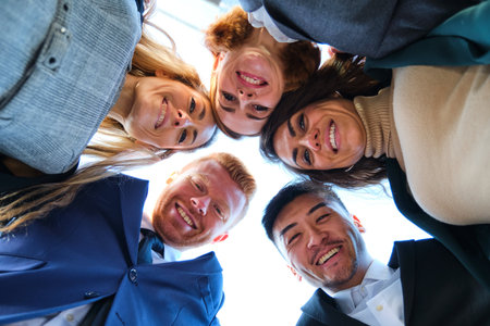 Low angle view of a group of international businesspeople together in circle looking at camera and smiling.の写真素材
