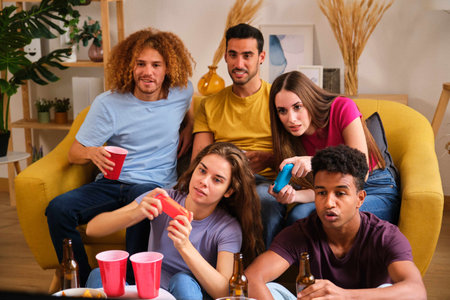 Multi ethnic friends sitting on sofa playing video games at a shared student flat.