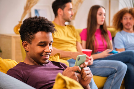 Young smiling Black man using his smartphone laying on the sofa at shared student flat.の写真素材