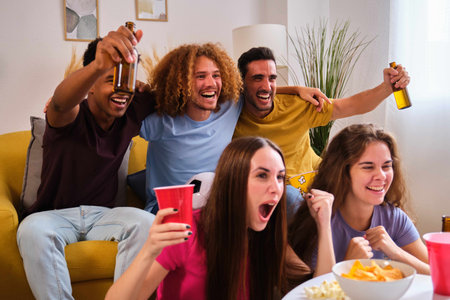Young friends celebrates a goal cheering for their soccer team watching the football match on TV.の写真素材