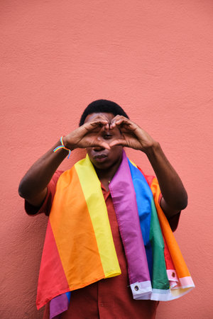 Gay black man wearing a rainbow flag holding his hands in a heart shape. Concept of unity and love...
