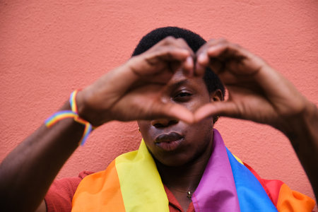 Gay black man wearing a rainbow flag holding his hands in a heart shape. Concept of unity and love...