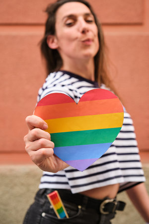 Trans lesbian woman holding a rainbow heart proudly in her hand during International Pride Month.