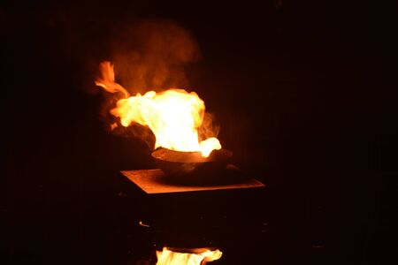 Flames of a huge bonfire at night near lake with bright orange fire reflecting in calm water surface against dark skyの写真素材