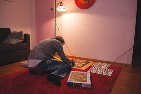 Man in white and black shirt doing puzzle in his living room. Entertainment conceptの写真素材