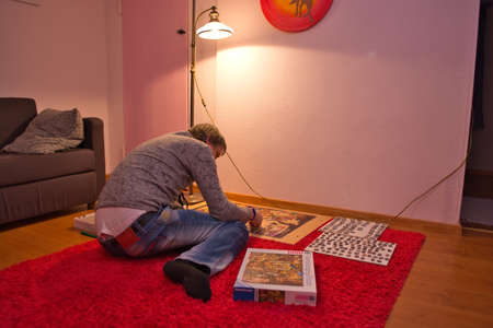 Man in white and black shirt doing puzzle in his living room. Entertainment conceptの写真素材
