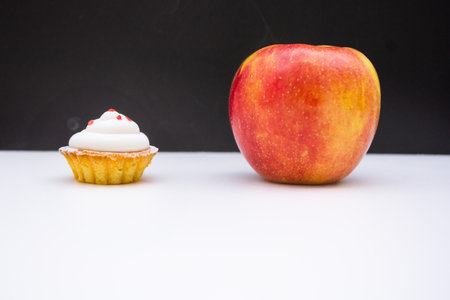 cup cake and an apple for diet struggle and confusion and decision for healthy eating and weight loss concept nutrition choices dilemmaの写真素材