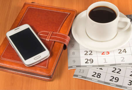 coffee, mobile phone,  planner and calendar on a wooden table.