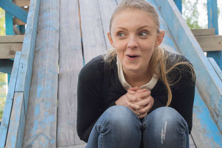 beautiful blonde girl making faces, sitting on a slide.