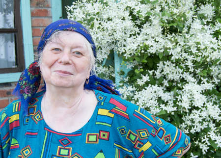 Smiling elderly woman in a kerchief on background of white flowers in your garden.