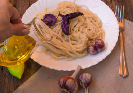 spaghetti with Basil, garlic, lady's hand holding a glass pitcher of olive oil.の写真素材
