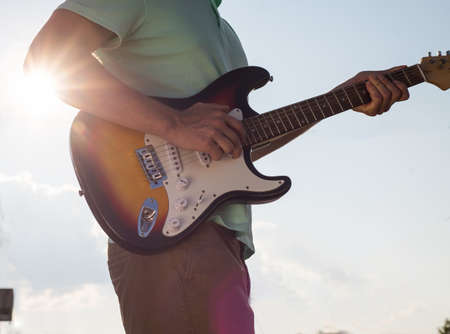 young man standing with a guitar on a background of sky and sunlightの写真素材