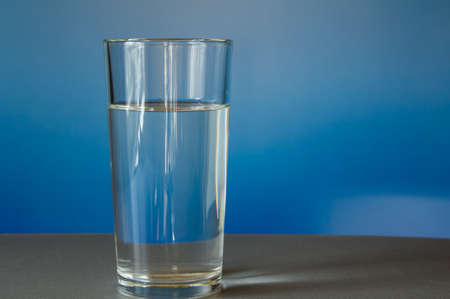 glass of water is on the table, blue background.