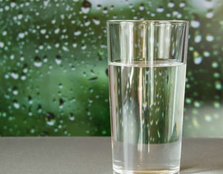 glass of water stands on a blurred green background with drops.