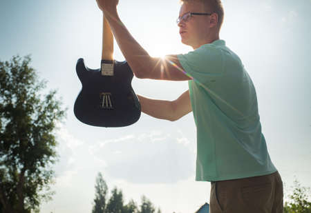 young man standing with a guitar on background of sky and sunlight.の写真素材