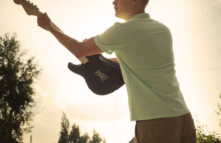 young man standing with a guitar on background of sky and sunlight.