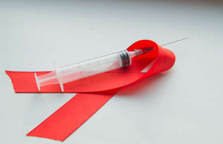 Awareness red ribbon and syringe on white background: world day against AIDS, the promotion of...