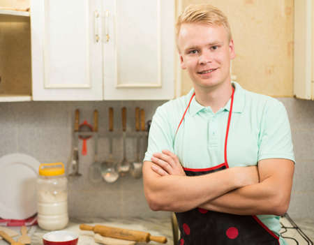 Happy smiling man standing in the kitchen with folded hands.の写真素材