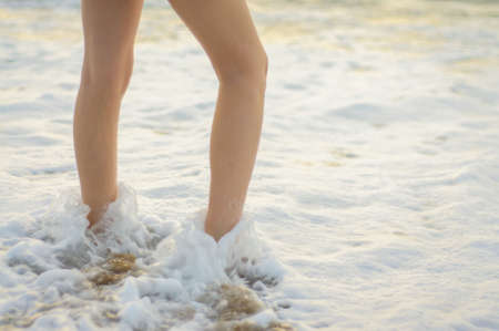 Legs of a young girl on sea and sandy beach.の写真素材