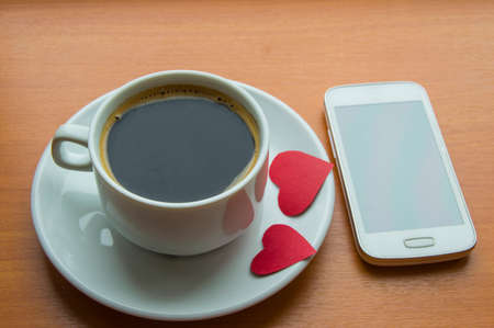Cell phone, coffee Cup with red hearts on a wooden tableの写真素材