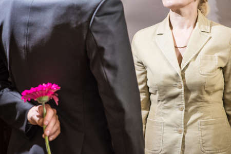 closeup of a man hiding a flower behind from womenの写真素材