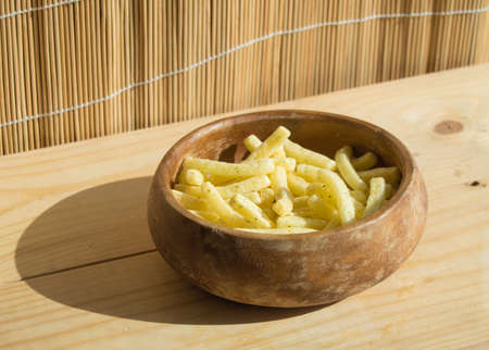 French fries in a wooden bowl, on a wooden background.