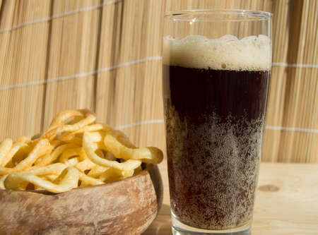 Plate of chips, a glass of dark beer with foam, bubbles on wooden backgroundの写真素材