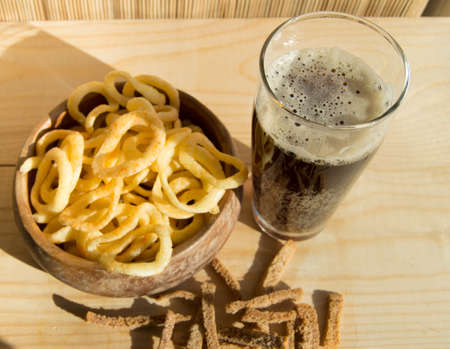 Plate of chips, glass of dark beer with foam, bubbles and crackers on wooden background Top viewの写真素材