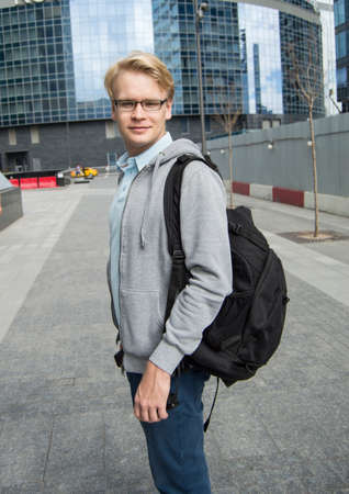Portrait of young attractive man with a backpack on the street near modern business center