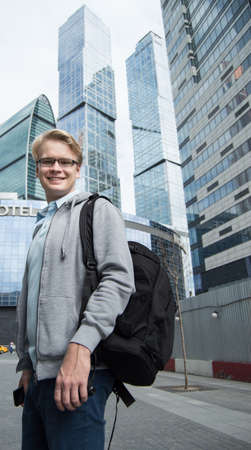Portrait of young attractive man with a backpack on the street near modern business centerの写真素材