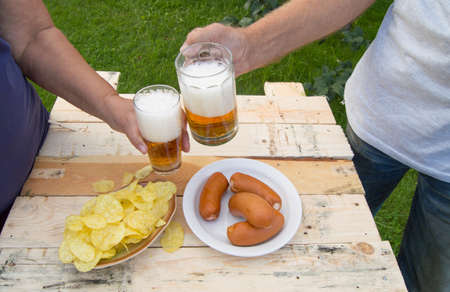 Hands holding glasses with beer, chips and sausages lying on a light wooden boards, people relax in the weekends, Octoberfestの写真素材