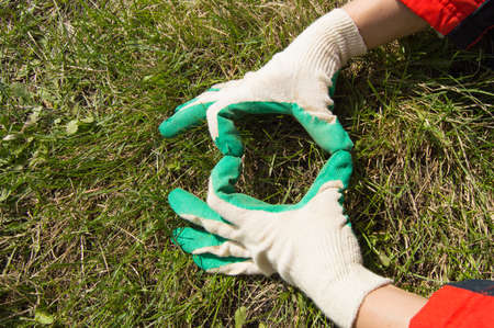 the woman in work gloves shows sign heart, on grass backgroundの写真素材