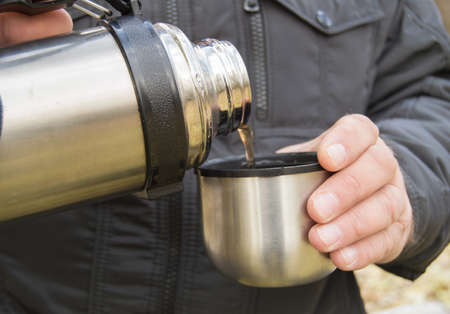 man in the Park in autumn pours hot coffee, tea from a bottleの写真素材