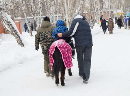 Happy family for a walk in Park-father teaches a young child to ride a ponyの写真素材