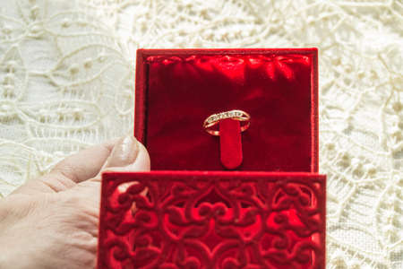 Female hand holding a red box with a ring on the background of the lace napkin, selective focusの写真素材