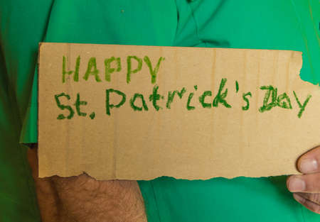 An elderly man in a green shirt holding a torn paper with the text of St. Patricks Day.の写真素材