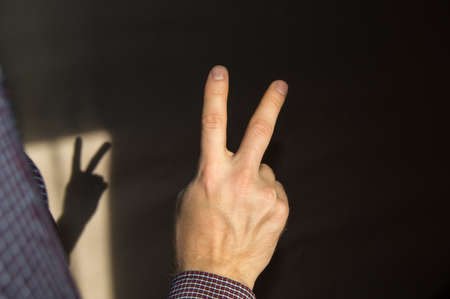 man raises two fingers up, showing a sign of victory, the view from the backの写真素材