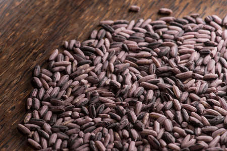 Dark purple rice on dark wooden background, top view, back-lit by sunlightの写真素材