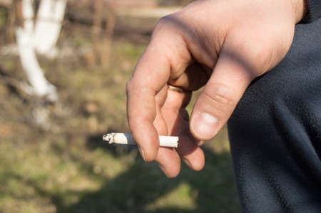 A young man holding a cigarette in his hand, sitting outdoorsの写真素材
