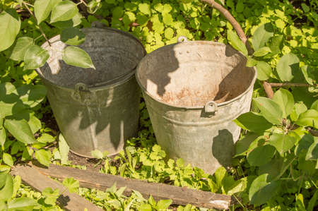 Two old rusty iron buckets in the garden grass.の写真素材
