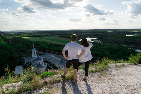 young couple travels standing on a hill and admiring the magnificent views of the valley, river and...