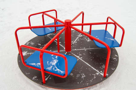 Round metal carousel for children in red and blue, white snow background.の写真素材