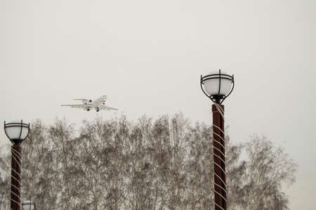 The plane flies low over the city Park and trees, cloudy winter sky. Copy space business travel...
