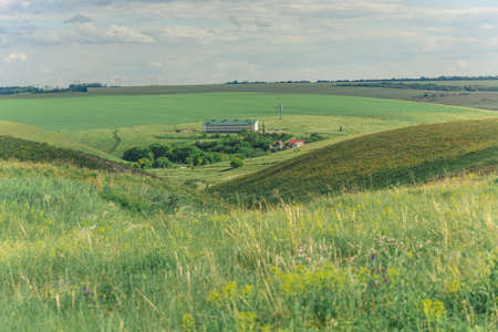 Summer landscape with hills and ravines overgrown with grass and blue sky with clouds