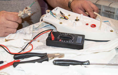 Close-up of the old electricians hand, the use of digital voltmeter for voltage to repair the...