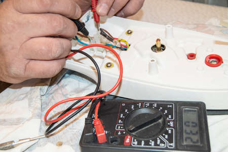 Close-up of the old electricians hand, the use of digital voltmeter for voltage to repair the electric iron, selective focusの写真素材