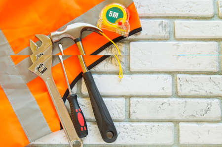 Flat lay composition with protective construction vest and working tool on brick wall background
