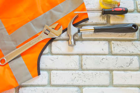 Flat lay composition with protective construction vest and working tool on brick wall background