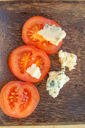 Italian culinary ingredients sliced tomatoes and cheese with mold on a dark rustic wooden plate, top viewの写真素材