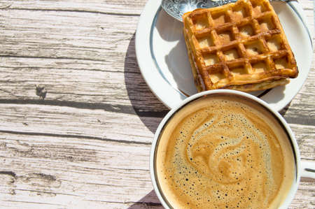 Soft Viennese waffle on a plate, a Cup of coffee on a wooden background, top view, copy space, flat...